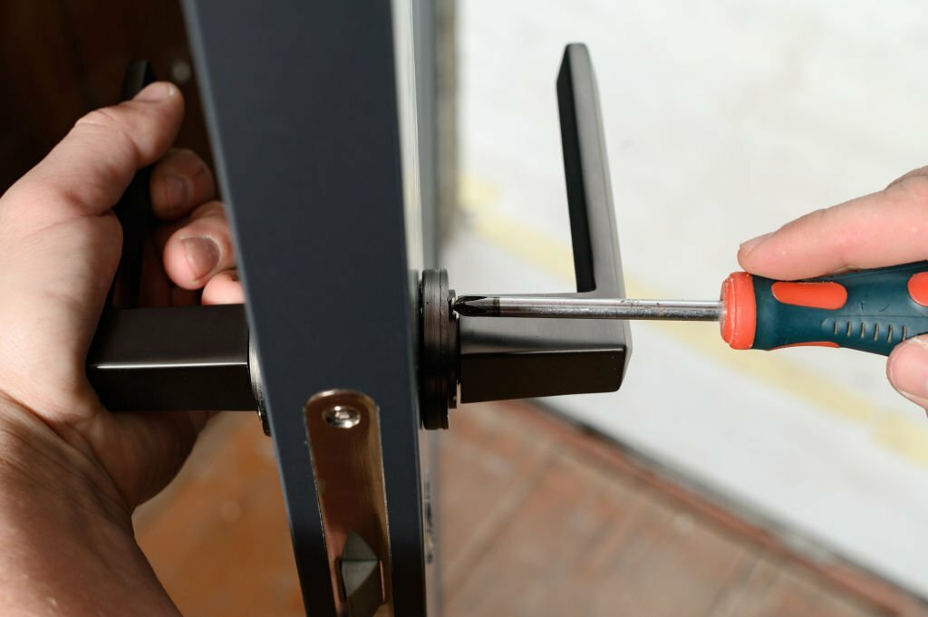 A man installs a door handle in a door, carpentry work at home, repair and restoration work.