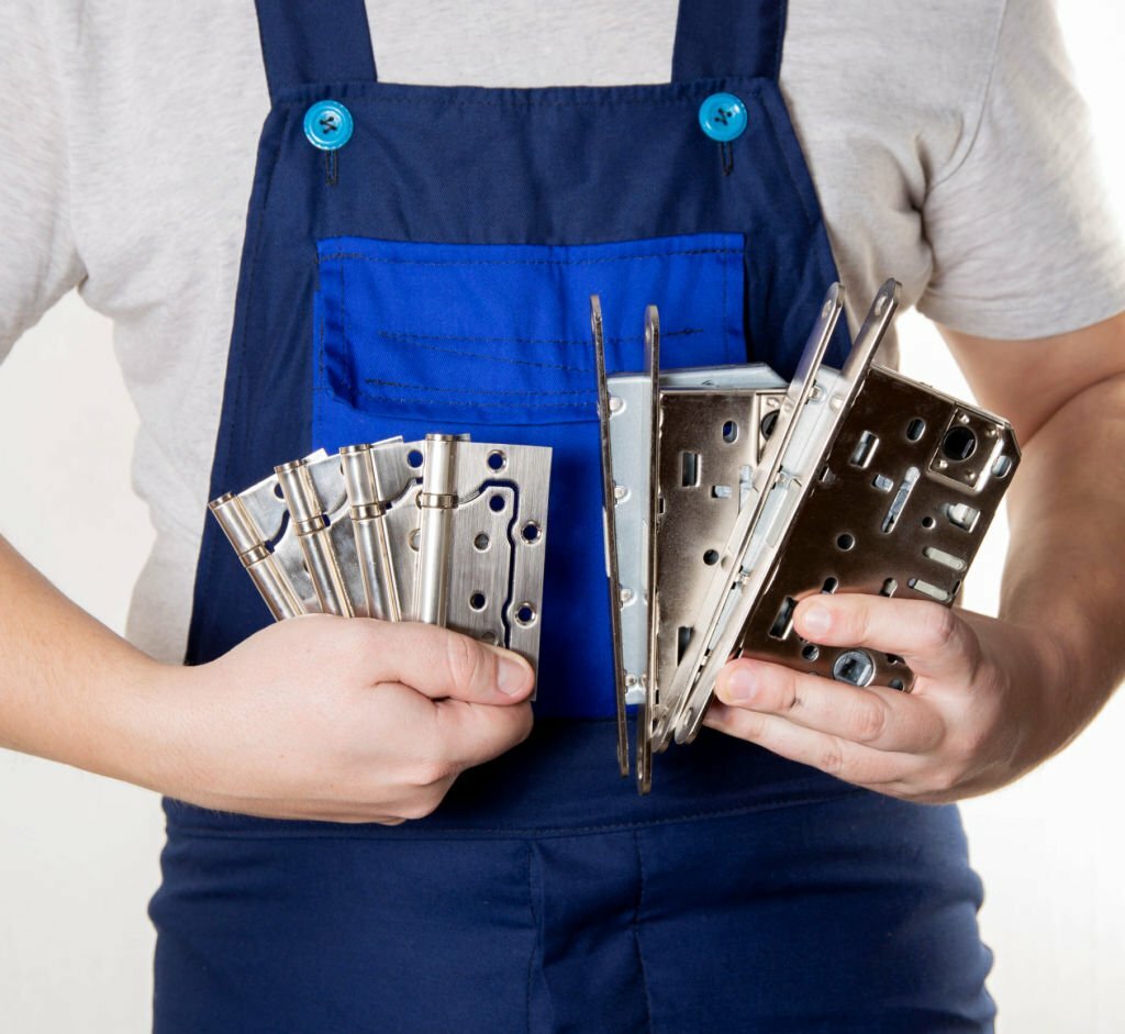 door installer holds door fittings in hands. Magnetic latch and door hinges on the background of blue overalls.