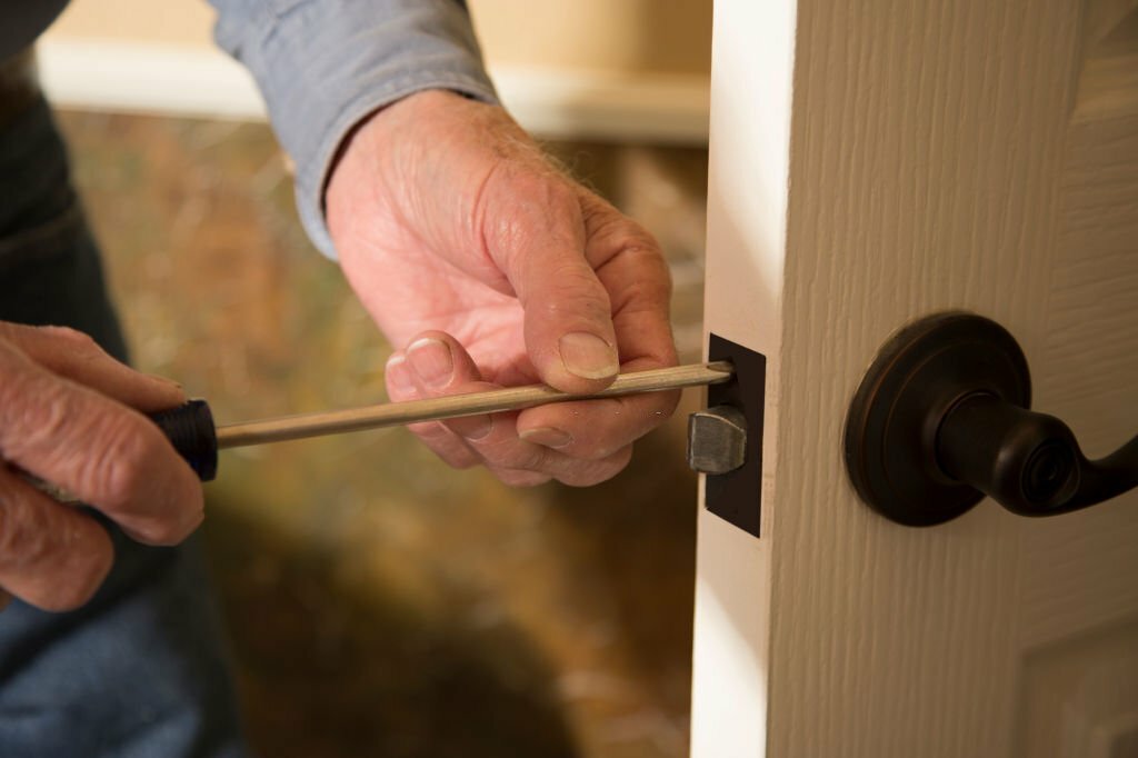 Worker in blue uniform or homeowner installing or repairing door knob on an interior door in the home.