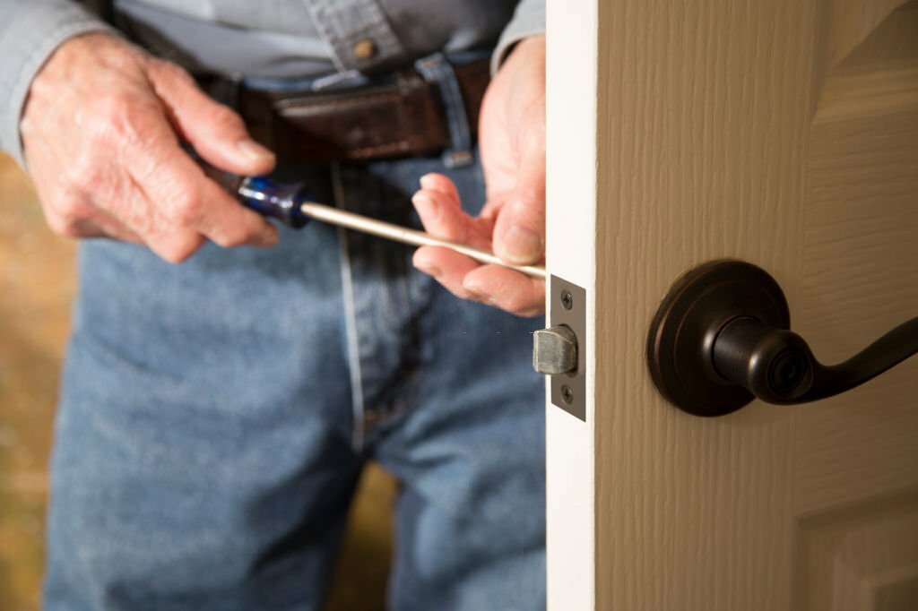 Worker in blue uniform or homeowner installing or repairing door knob on an interior door in the home.