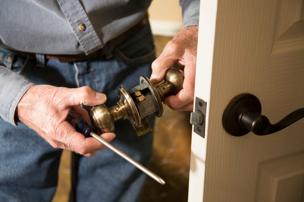 Worker in blue uniform or homeowner installing or repairing door knob on an interior door in the home.